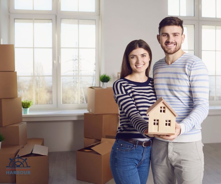 Building and Contents insurance a young couple hold a wooden house in their hands, stood in an empty room filled with boxes