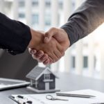 Mortgage Products t male hands shaking over a desk with a model house on it